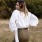 Woman wearing a white tie-neck blouse with voluminous long sleeves, styled with a green plaid midi skirt.