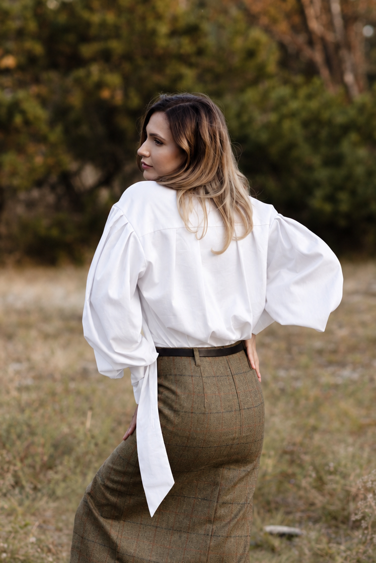 Woman wearing a white tie-neck blouse with voluminous long sleeves, styled with a green plaid midi skirt.