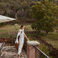 Woman wearing a white linen midi dress with long shoulder ties on a balcony
