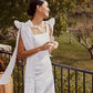 Woman wearing a white linen midi dress with shoulder bows standing on a terrace