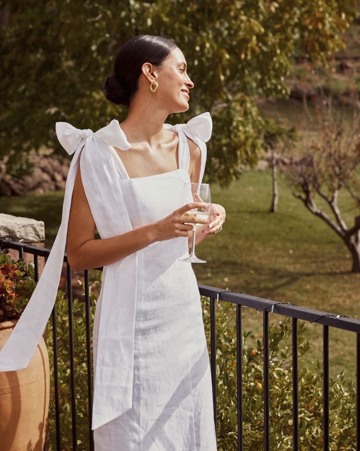 Woman wearing a white linen midi dress with shoulder bows standing on a terrace