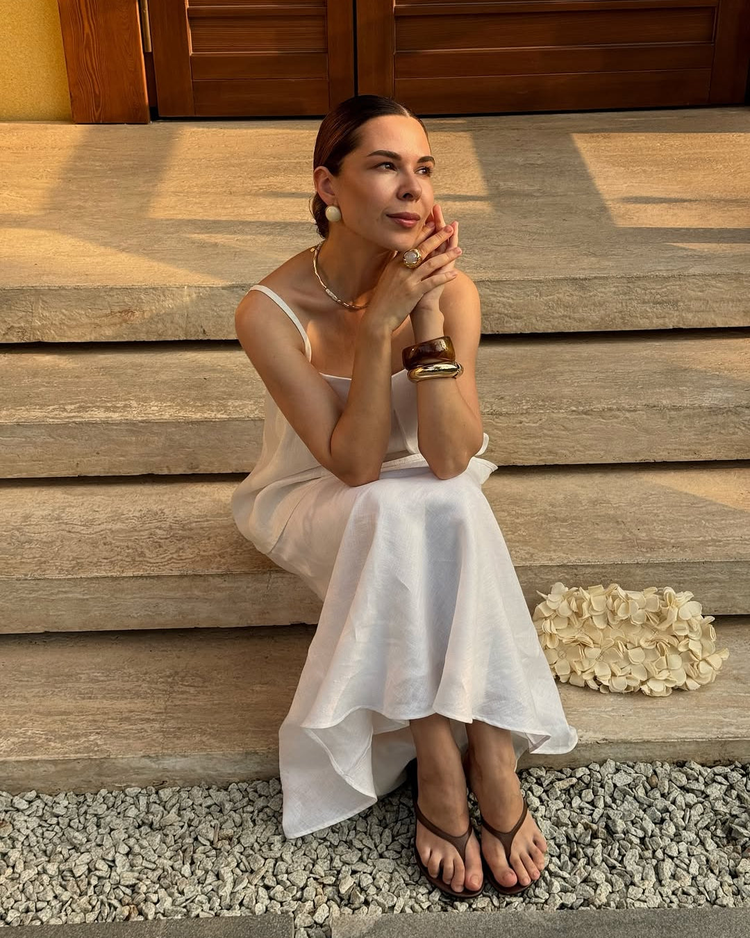 Woman in a white linen skirt and top sitting on wooden steps outdoors