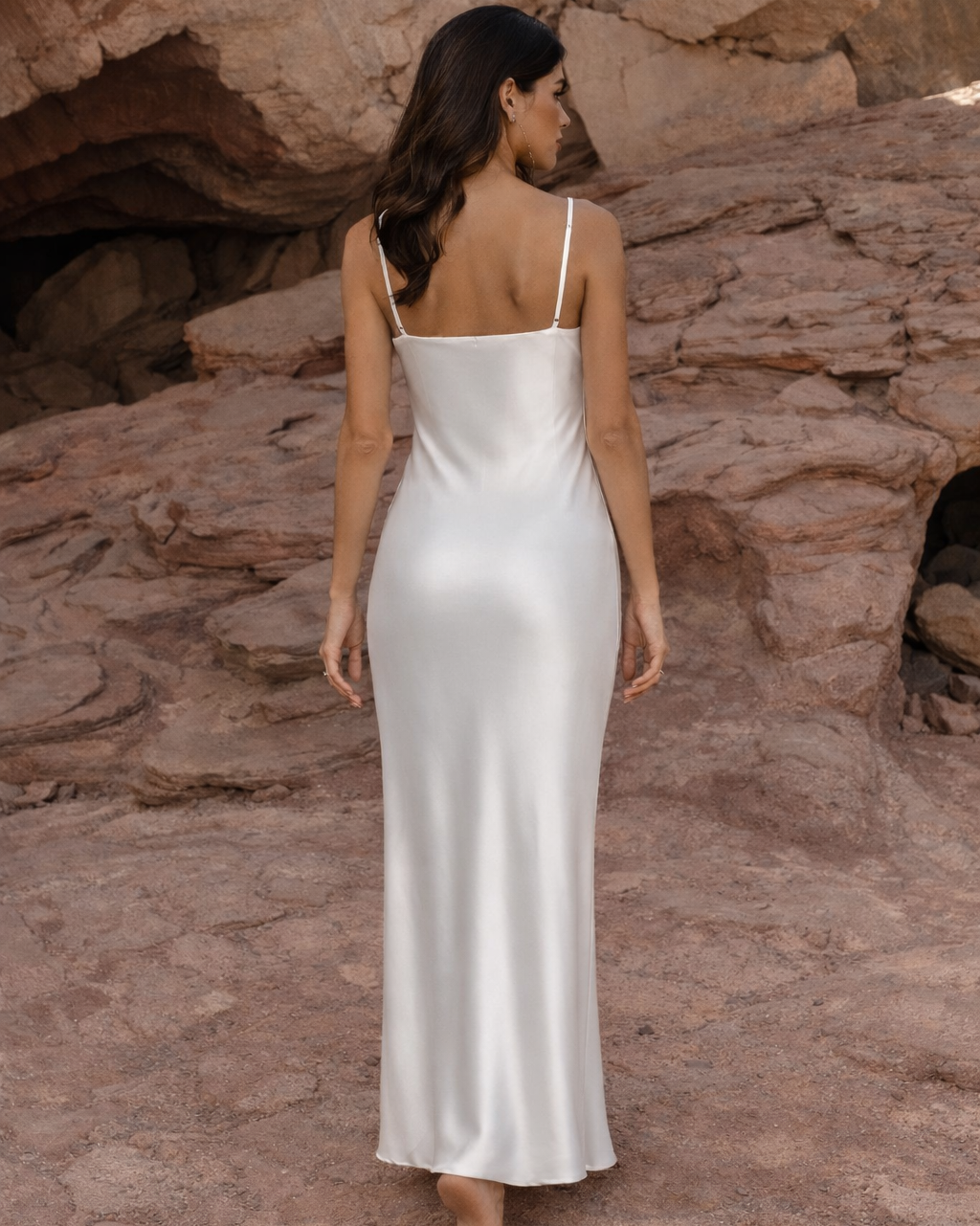 Full length back view of a woman wearing a white silk slip dress with thin straps
