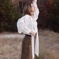 Side view of a white tie-neck blouse with shoulder draping, voluminous sleeves and long ascot ties.