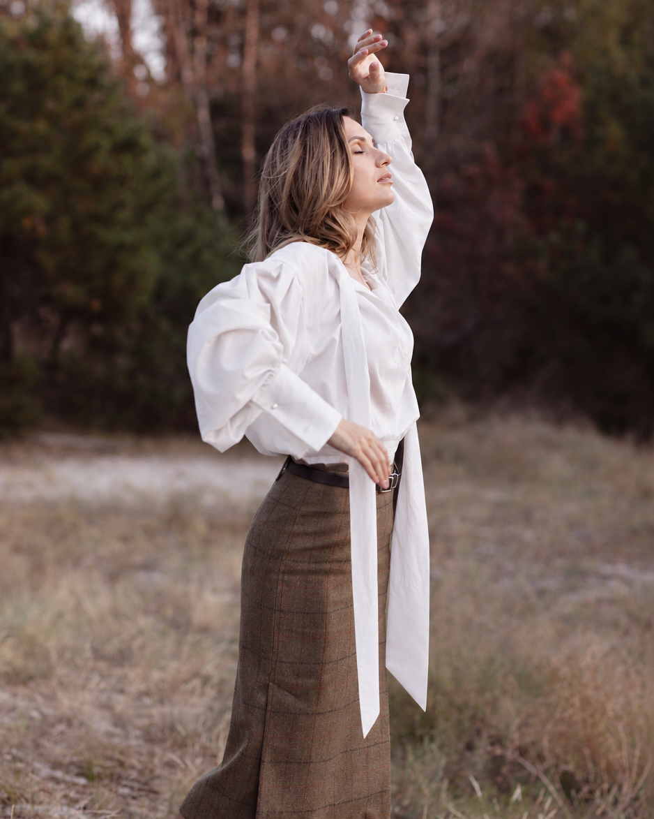 Side view of a white tie-neck blouse with shoulder draping, voluminous sleeves and long ascot ties.