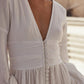 Close-up of the white muslin wedding dress showing the deep V-neck, draped waist and fabric-covered front buttons.