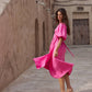A woman wearing a bright pink midi dress with puff sleeves and a matching tie belt.