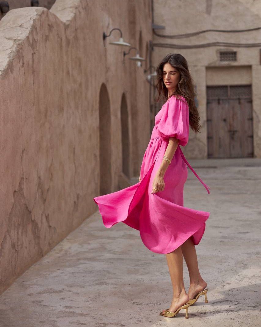 A woman wearing a bright pink midi dress with puff sleeves and a matching tie belt.