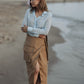 A woman standing on a beach wearing a beige wrap midi skirt with a utility pocket detail, paired with a light blue shirt.