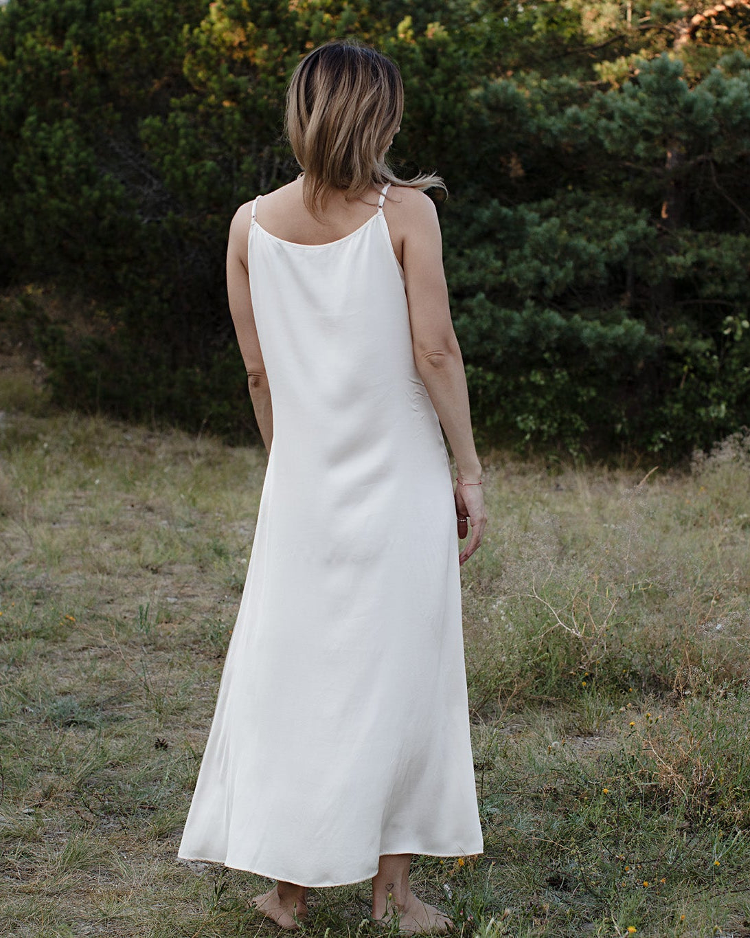 Person wearing a ivory dress standing in a natural setting with greenery.