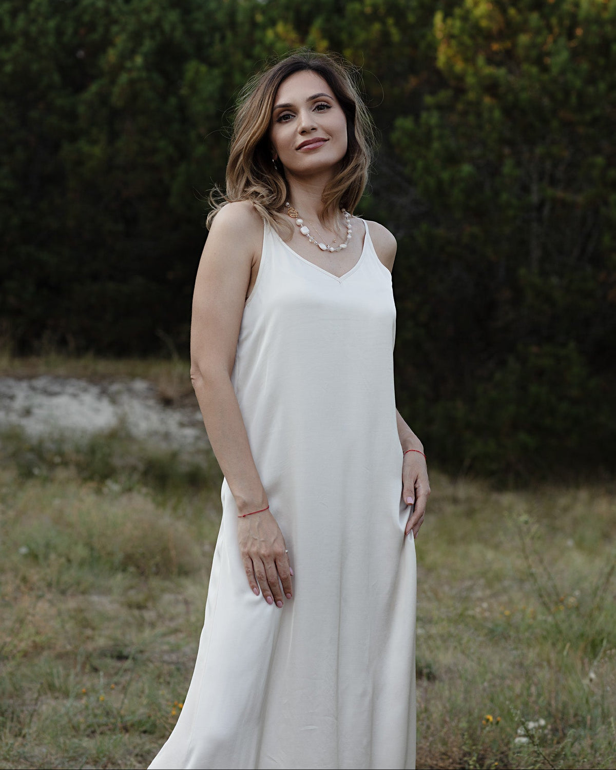 Woman in a ivory dress standing in a natural setting with greenery.