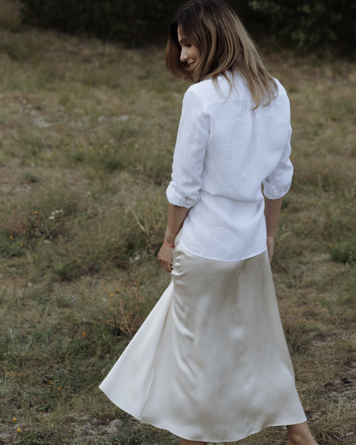 Woman in a white blouse and beige skirt standing in a grassy field.
